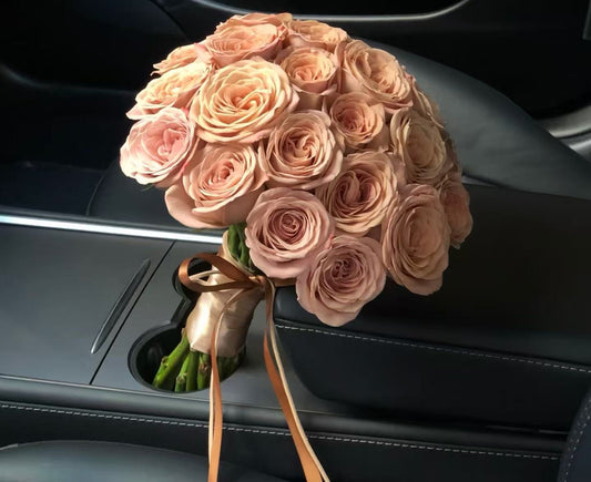 A bouquet of peach-pink roses tied with a brown ribbon, resting in a car cup holder.